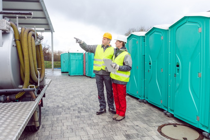 Two technicians reviewing a delivery in front of a row of Countrywide Rental portable restrooms, with a service truck alongside